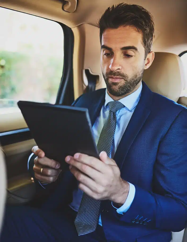 Geschäftsmann sitzt in einem PKW und hält ein Tablet in der Hand